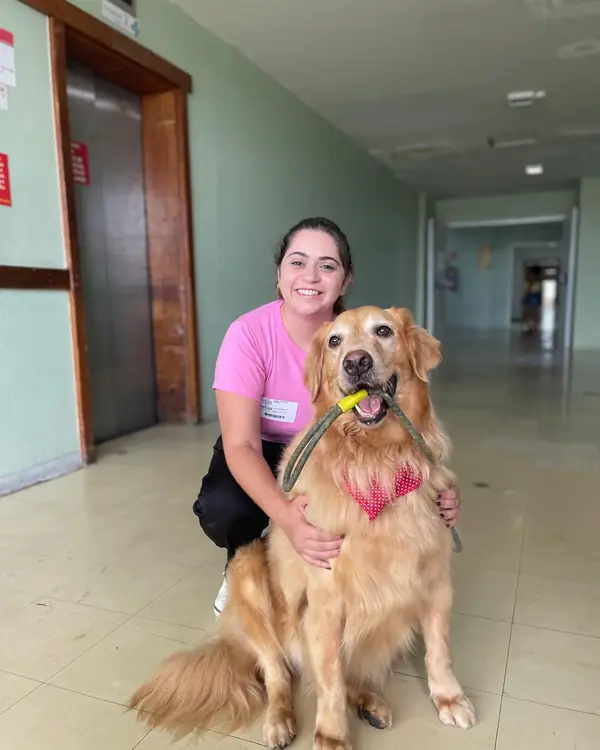 Dra. Laís Rosseto agachada ao lado de um golden retriever segurando a guia na boca